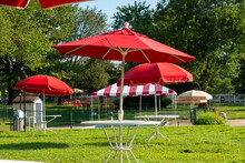 Grassy Area With Several Small White Picnic Tables With Red Umbrellas