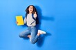 © Krakenimages.com - Young beautiful chinese student girl wearing glasses and backpack smiling happy. Jumping with smile on face holding book doing ok sign over isolated blue background
