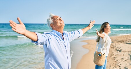 Canvas Print - Middle age hispanic couple breathing with arms raised at the beach.