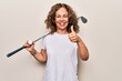 Middle age beautiful sportswoman playing golf using stick and ball over white background smiling happy and positive, thumb up doing excellent and approval sign