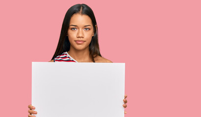 Canvas Print - Beautiful hispanic woman holding blank empty banner thinking attitude and sober expression looking self confident