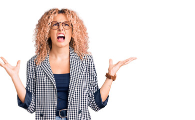 Young blonde woman with curly hair wearing business jacket and glasses crazy and mad shouting and yelling with aggressive expression and arms raised. frustration concept.