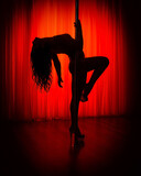 Pole dance. Silhouette of sexy woman dancing on a pole in the interior of a nightclub with a red background.