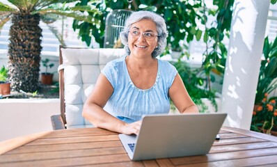 Wall Mural - Middle age woman with grey hair smiling happy relaxing sitting at the terrace working from home