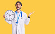 © Krakenimages.com - Handsome hispanic man wearing doctor uniform holding clock celebrating victory with happy smile and winner expression with raised hands