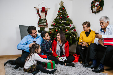 Wall Mural - Latin family giving presents on Christmas eve. Grandparents in Mexico observing their grandchildren