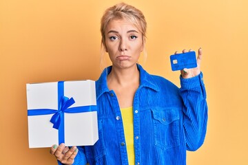 Poster - Young blonde girl holding gift and credit card depressed and worry for distress, crying angry and afraid. sad expression.