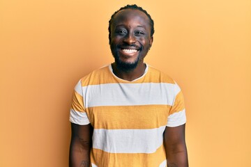 Canvas Print - Handsome young black man wearing casual yellow tshirt looking positive and happy standing and smiling with a confident smile showing teeth