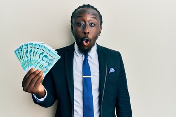 Poster - Handsome young black man wearing business suit holding 50 yuan banknotes scared and amazed with open mouth for surprise, disbelief face