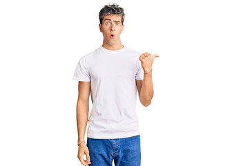 Young handsome man wearing casual white tshirt surprised pointing with hand finger to the side, open mouth amazed expression.