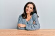 © Krakenimages.com - Young brunette woman wearing casual sweater sitting on the table happy face smiling with crossed arms looking at the camera. positive person.