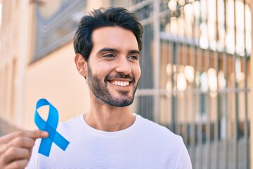 Young hispanic man smiling happy holding blue ribbon at the city.