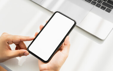 Canvas Print - Woman hand holding smartphone with blank copy space screen for your advertisement. laptop on the table.