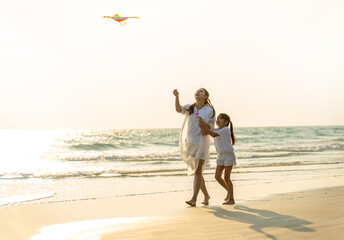 Wall Mural - Happy Asian family single mother with little daughter playing kite together on the beach at summer sunset. Beautiful mother and cute child girl relax and having fun in summer holiday vacation.