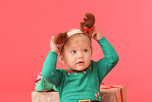 Cute Little Baby In Elf's Costume And With Deer Horns On Color Background