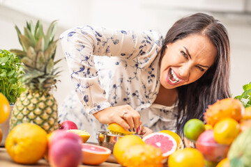 Wall Mural - Woman squeezing an orange hard at home with plenty of fruit around her