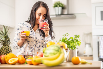 Wall Mural - Woman smells freshly squeezed juice from a cup in a kitchen full of fruit