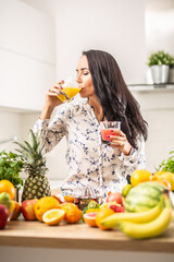 Woman drinking orange juice from a cup in the kitchen full of fruit