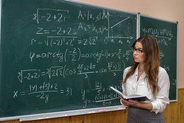 attractive female teacher in glasses near blackboard with math calculations