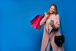 © Тарас Нагирняк - .Young beautiful blonde girl in a raincoat on a blue background with mobile phone doing online shopping