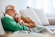 Elderly man and woman with flu. Couple of old aged senior people at home with seasonal winter cold illness disease sit down on the sof together forever - health problems for retired man and woman 