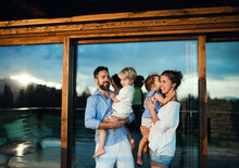 Family With Small Children Standing By Wooden Cabin, Holiday In Nature Concept.