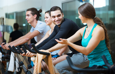 Group of happy adult people training on exercise bikes in gym