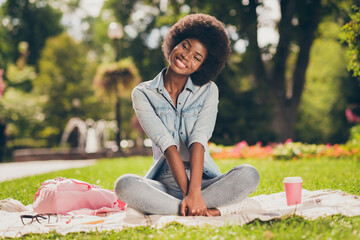 Poster - Photo portrait of black skinned cute young woman sitting in city green park near bag paper mug of hot beverage smiling cheerfully