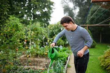 down syndrome adult man watering plants outdoors in vegetable garden, gardening concept.