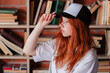 © oleg_ermak - Portrait of a redhead woman in template blank t-shirt and cap with healthy freckled skin. Young caucasian model posing on bookshelf background. Copy space and mock up. Place for adverising