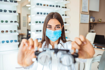 Wall Mural - Talented skillful optician choosing lenses for trial spectacles, Young beautiful girl ophthalmologist working on trial glasses in her ophthalmology clinic.