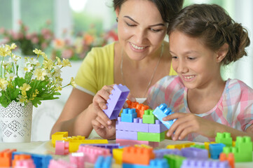 Poster - little daughter and mother playing with colorful plastic blocks at home