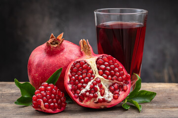 Healthy pomegranate drink in a transparent glass near ripe open pomegranate fruits on a dark background.