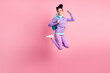 Full length photo of girl jump raise fists wear bag eyewear violet pullover pants sneakers isolated pink color background