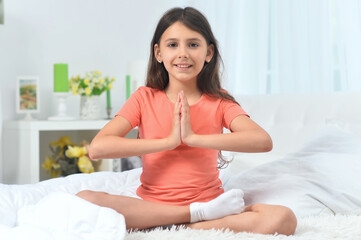 Wall Mural - Cute little girl doing yoga in bed