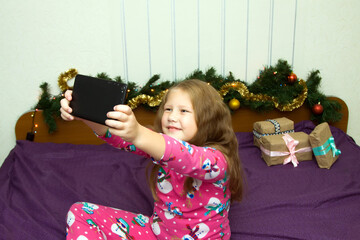 Christmas online congratulations. Smiling  girl woman 
dressed in christmas pajamas using mobile tablet for video call friends and parents.