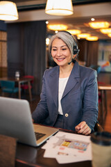 Cheerful woman wearing headset while using laptop at work