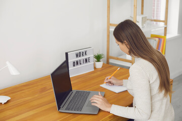 work online home.young woman sitting at laptop computer with blank screen and taking notes during on