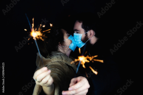 Young couple wearing protective face masks for Coronavirus and holding sparklers for New year\'s eve, 2021 and Covid-19 concept