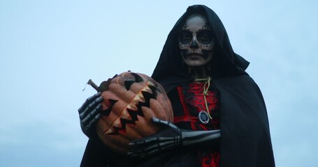 Wall Mural - Woman stands in Halloween costume of death and jack-o-lantern against background of sky.