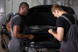 © alfa27 - multi-ethnic team of african and caucasian men working in auto service together, friendly men in uniform repair the car hood