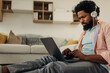 © bernardbodo - Young black man with earphones sitting on the floor and using laptop