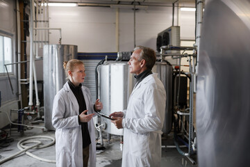 Side view portrait of mature man instructing female worker while discussing work at food production factory, copy space