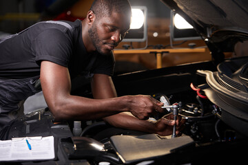 Wall Mural - african professional auto service technician in uniform standing near car hood repairing and using check list for car inspect, indoors