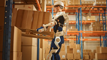High-Tech Futuristic Warehouse: Worker Wearing Advanced Full Body Powered Exoskeleton, Lifts Heavy Pallet Full Of Cardboard Boxes. Delivery Exosuit Amplifies Strength.