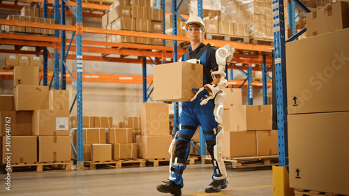 High-Tech Futuristic Warehouse: Worker Wearing Advanced Full Body Powered exoskeleton, Walks with Heavy Cardboard Box. Delivery Exosuit amplifies Human strength.