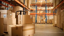 Big Retail Warehouse Full Of Shelves With Goods Stored On Manual Pallet Truck In Cardboard Boxes And Packages. Forklift Driving In Background. Logistics And Distribution Facility For Product Delivery