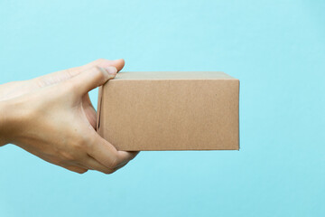 Wall Mural - Woman hand hold the brown corrugated box on blue  wall background with copy space