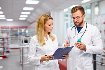 Wall Mural - two young professional druggists colleagues fulfilling a prescription holding medication in hand, checking the script