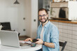 © ViDi Studio - Smiling man in glasses sit at table in coffee shop cafe restaurant indoors working studying on laptop computer pay off with cell phone bank payment terminal. Freelance mobile office business concept.